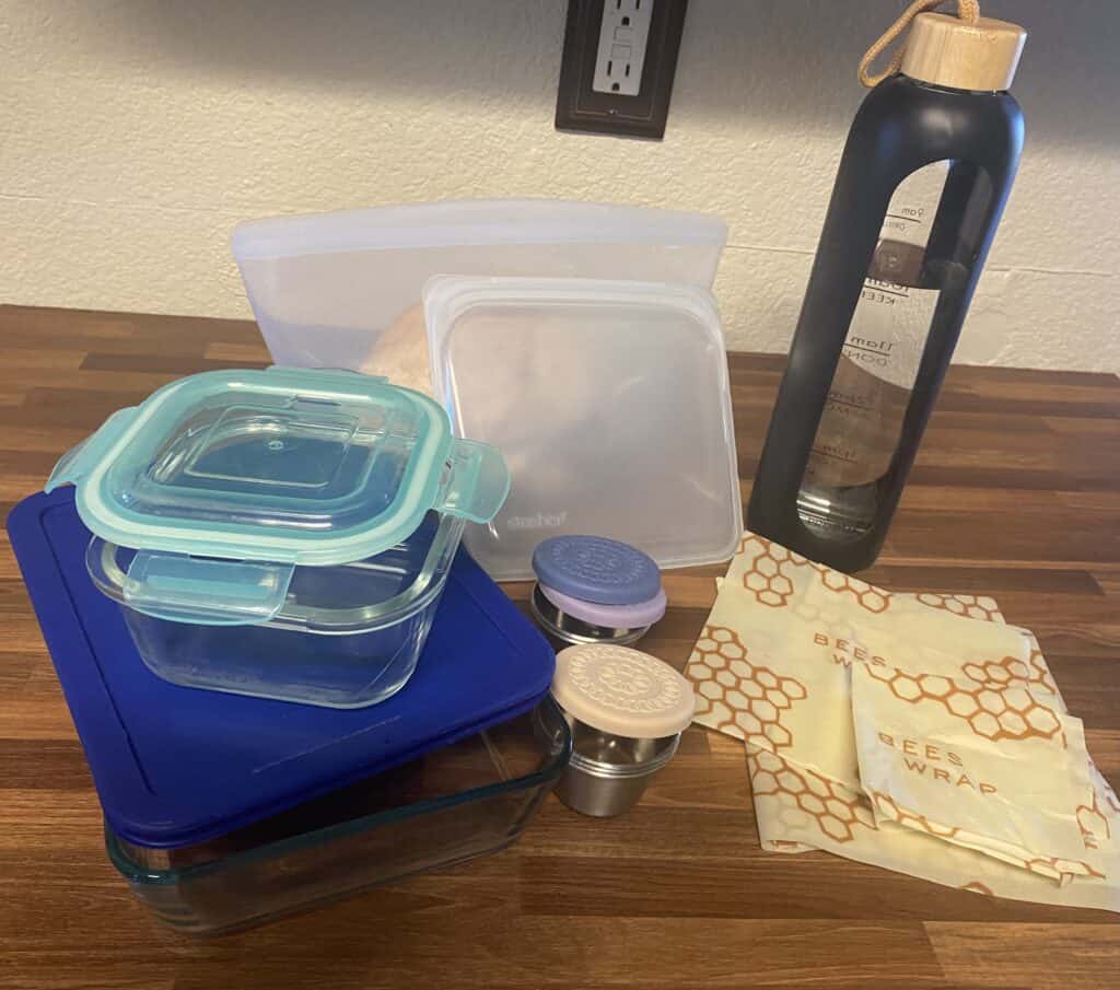 a glass water bottle, glass and stainless steel food containers, silicone ziploc bags, and beeswax paper