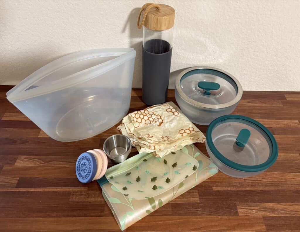 non toxic food containers including a glass water bottle, stainless steel condiment containers, reusable silicone ziplock bags, and wax paper.