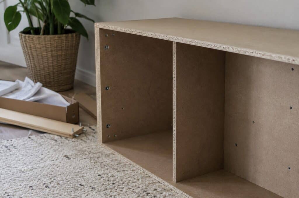 Partially assembled particleboard bookshelf on a carpeted floor with unpacked hardware and instructions nearby, showing engineered wood materials that commonly contain formaldehyde-based adhesives.