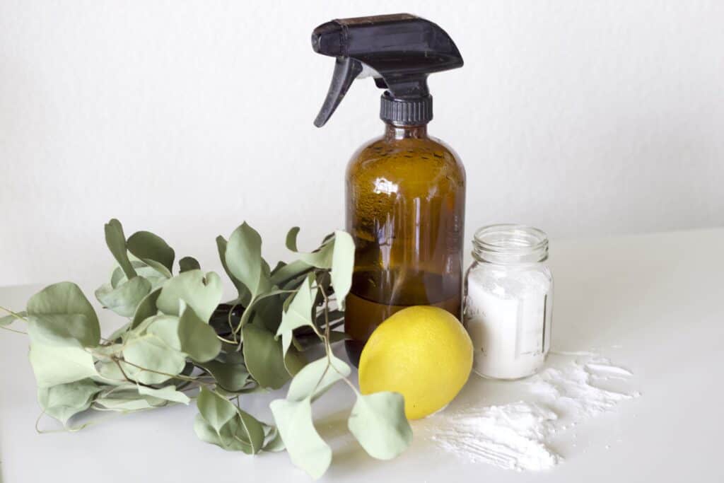 a spray bottle next to a lemon and glass jar of baking soda