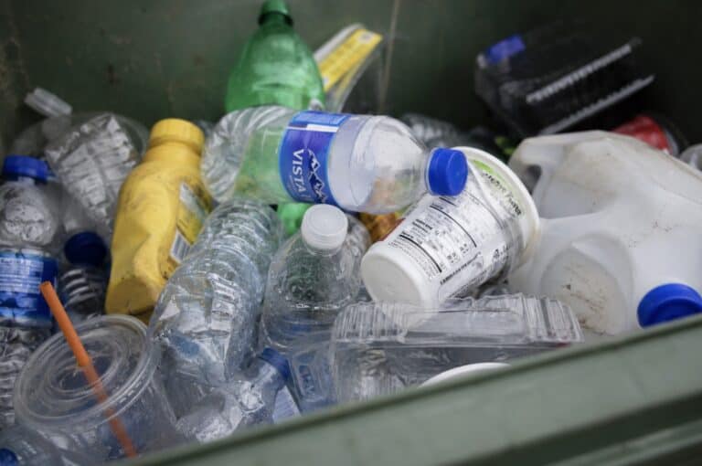 Close-up of a recycling bin filled with used plastic bottles, food containers, and plastic packaging, illustrating common household plastic waste and disposal.