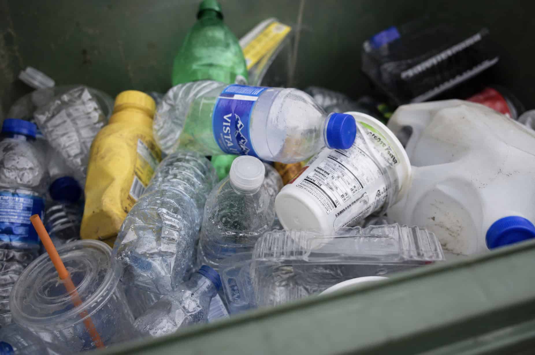 Close-up of a recycling bin filled with used plastic bottles, food containers, and plastic packaging, illustrating common household plastic waste and disposal.