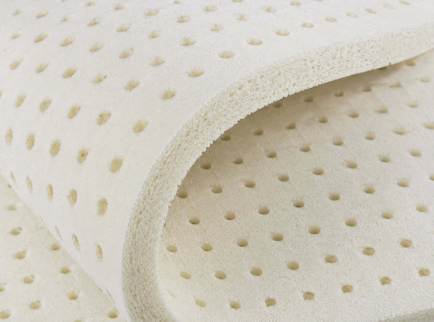 Close-up of a piece of synthetic latex foam with evenly spaced ventilation holes and a flexible curved edge, commonly used in mattresses and cushions.