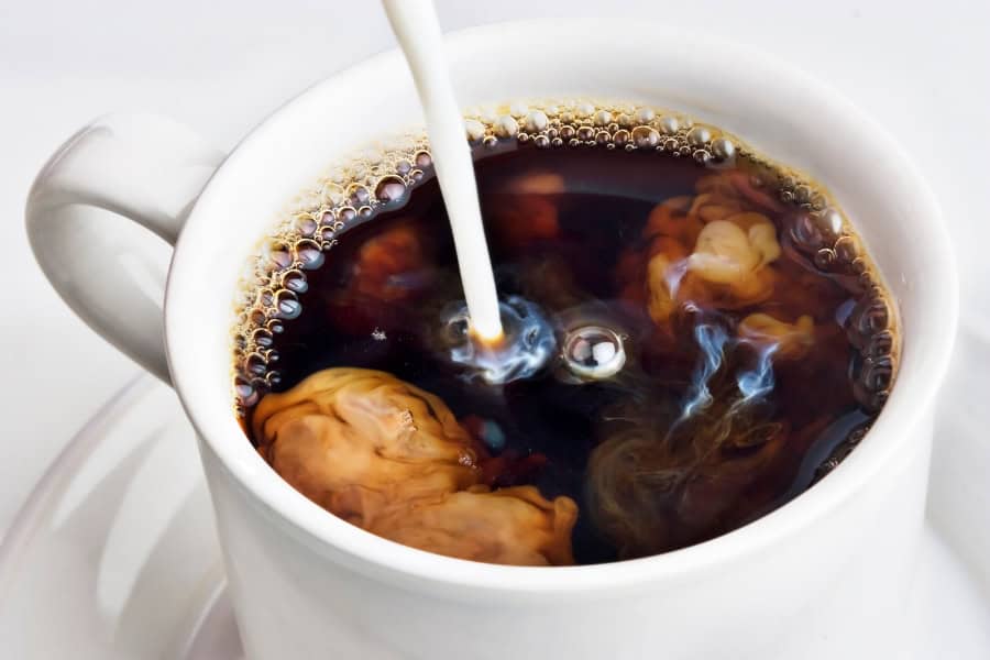 cup of hot coffee with creamer being poured into it