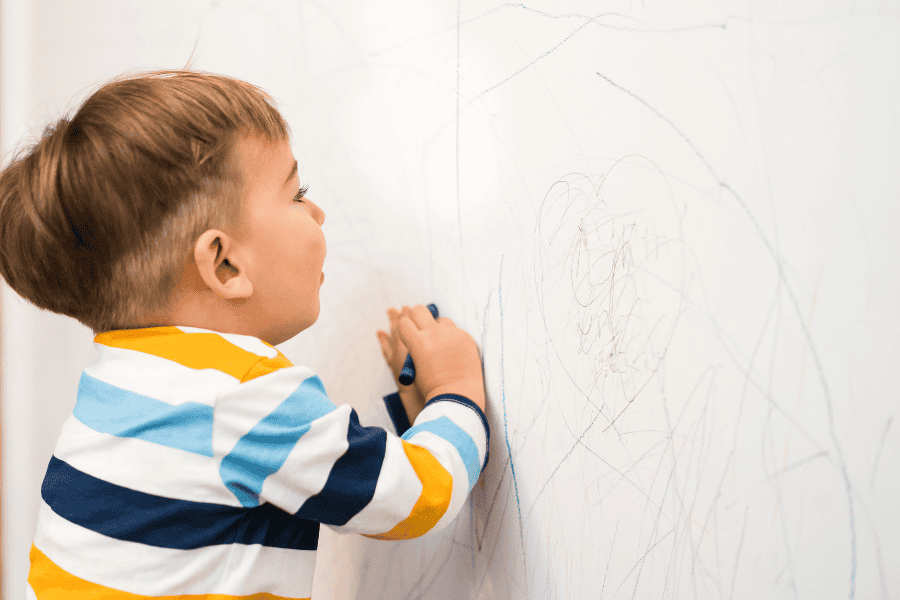 a child drawing on the wall with crayon