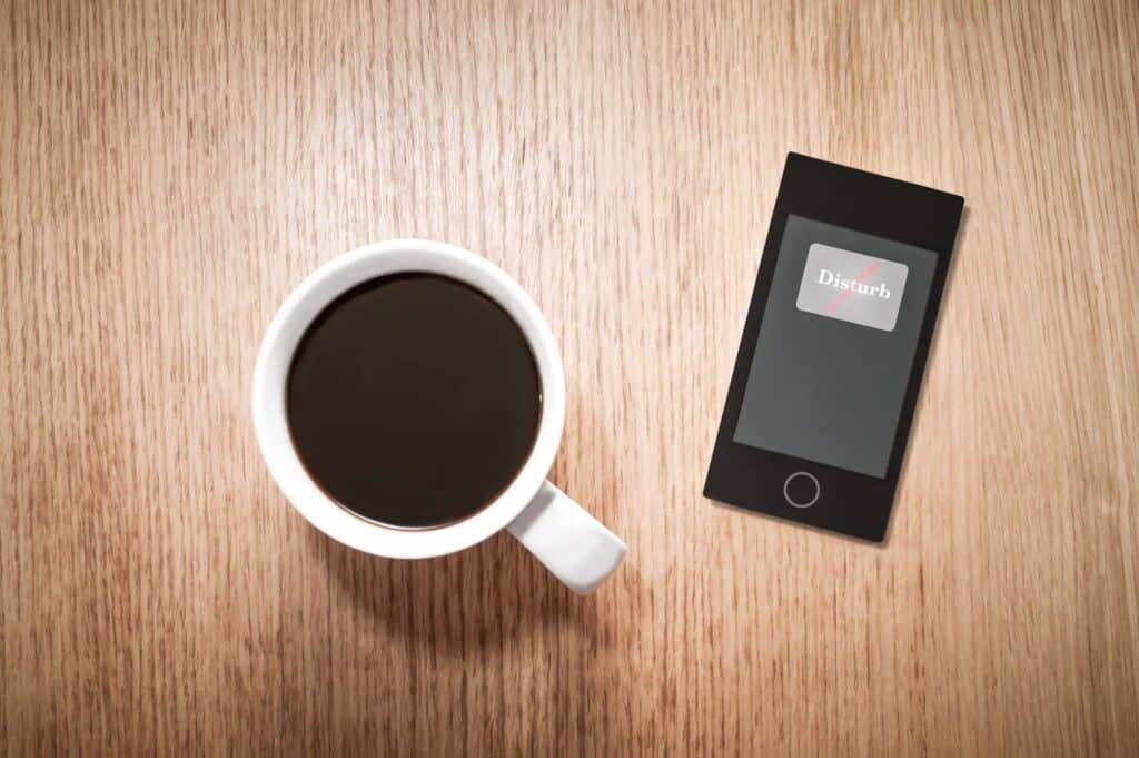 a cup of coffee next to a phone set to "do not disturb"