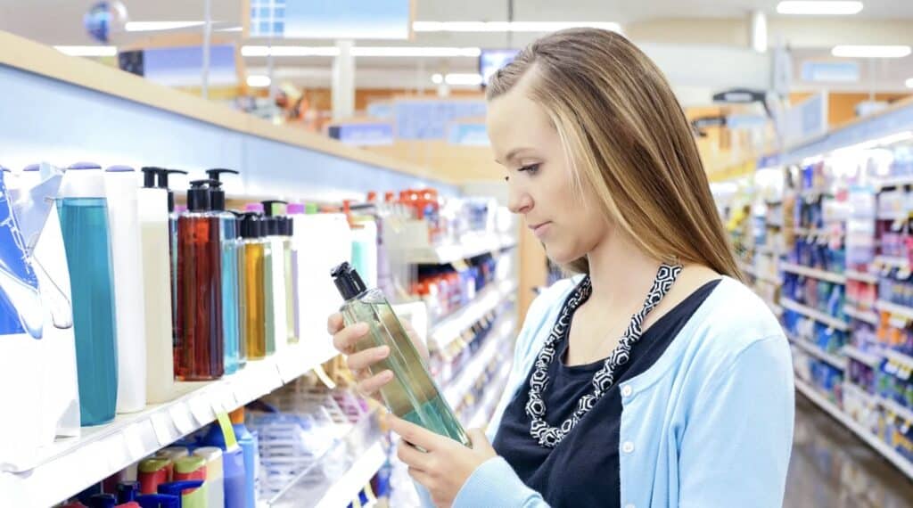 a woman looking at the ingredients on a shampoo bottle while shopping