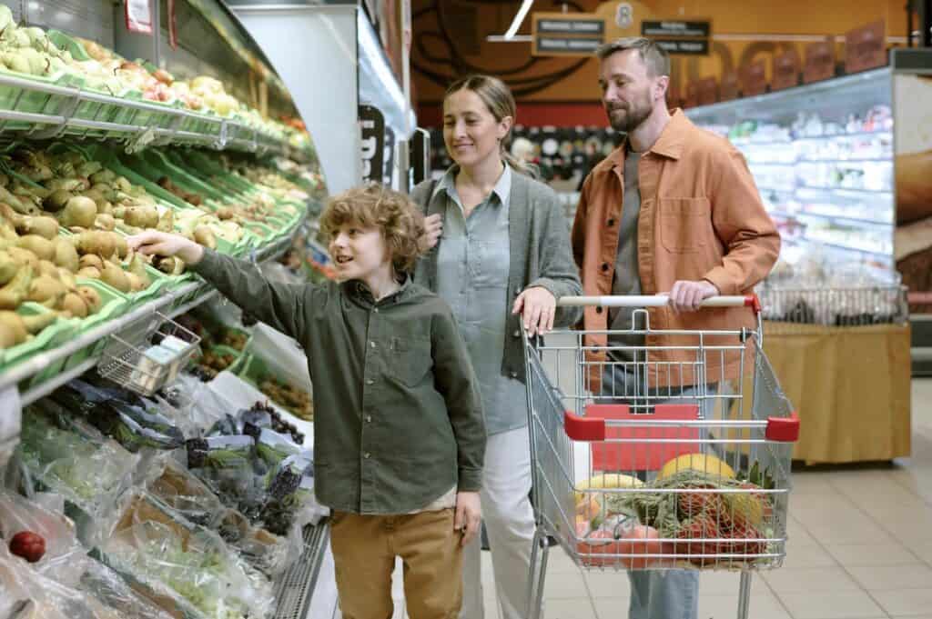 Family shopping for fresh produce in a grocery store while selecting fruits and vegetables from the produce aisle.
