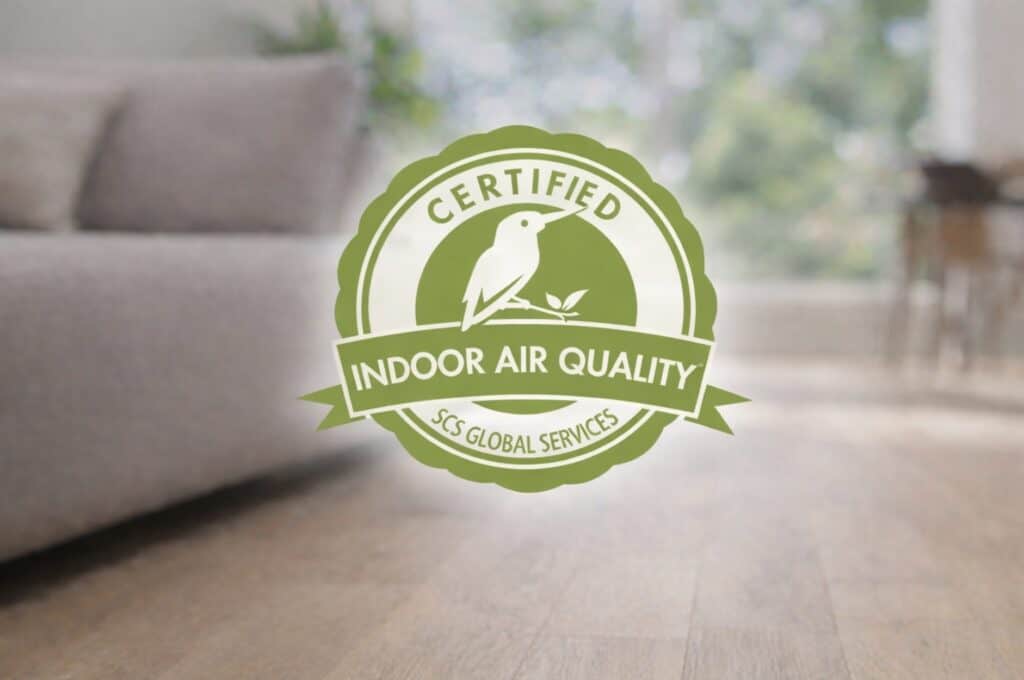SCS Indoor Advantage Gold certification logo centered over a blurred living room background with light wood flooring and a beige sofa