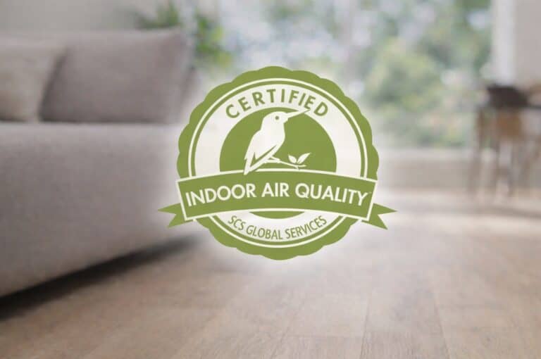 SCS Indoor Advantage Gold certification logo centered over a blurred living room background with light wood flooring and a beige sofa