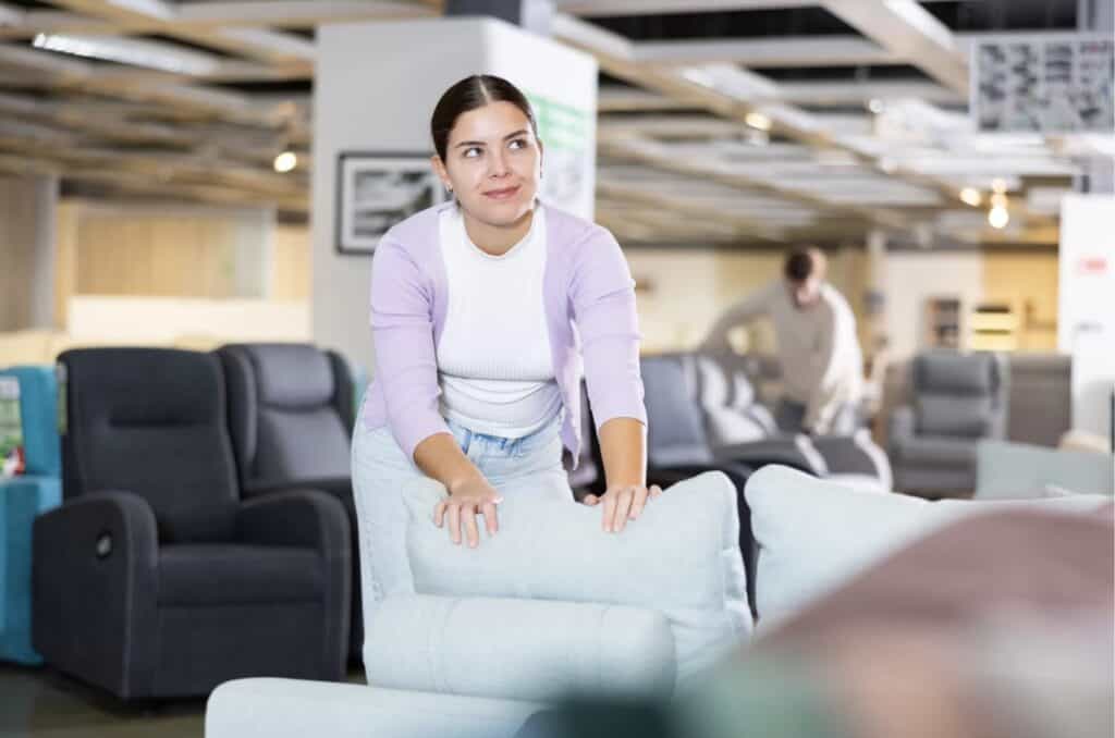 Woman testing a sofa in a furniture store showroom while comparing upholstered couches and seating options.