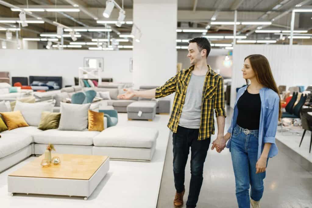 Couple walking through a furniture showroom while looking at sofas and living room furniture displays.