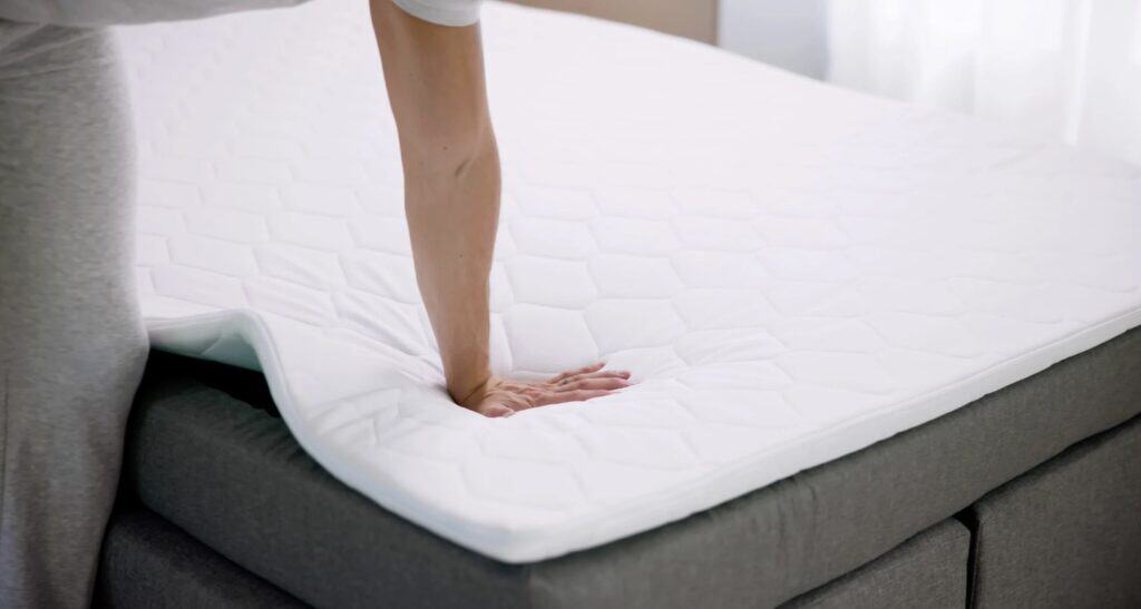 Hand pressing into a white memory foam mattress, showing its soft, contouring support on a bed.