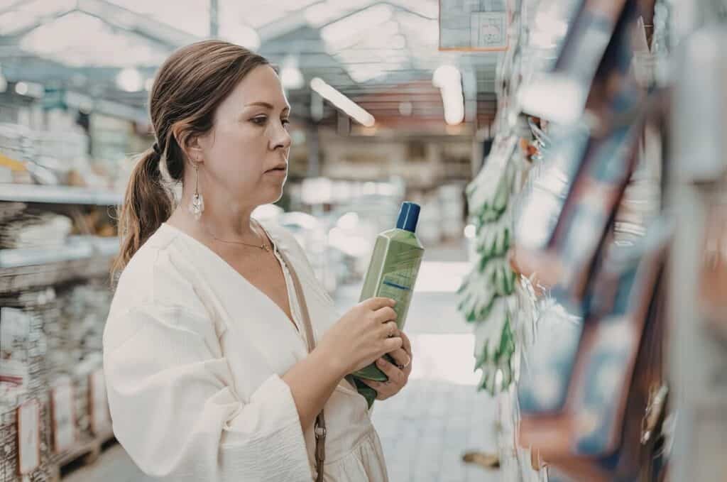 Woman standing in a store aisle comparing household cleaning products on a shelf
