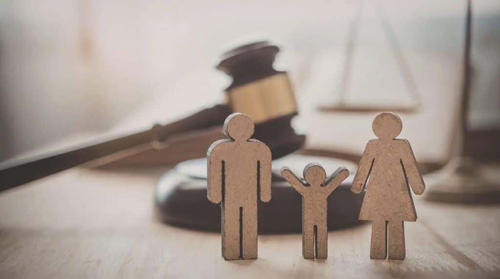 Wooden family figures in front of a judge’s gavel and scales of justice, symbolizing family law or legal protection