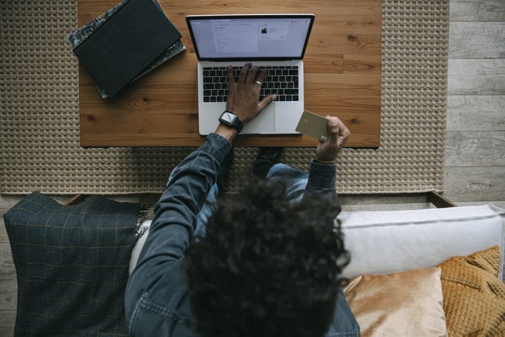 Person shopping online on a laptop while holding a credit card at a wooden table