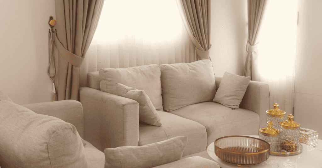 beige upholstered sofa in a bright living room with neutral curtains