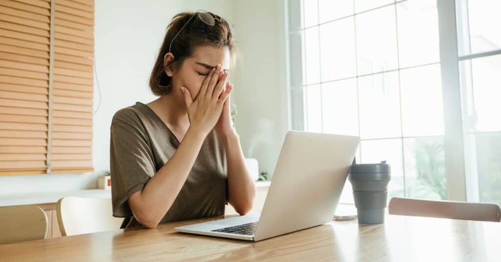 Tired person rubbing eyes while sitting in front of a laptop