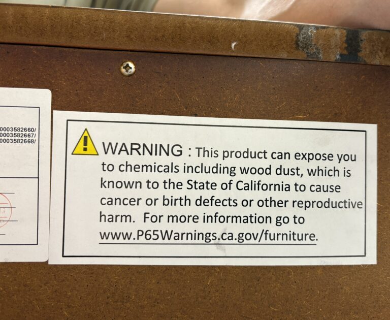 Close-up of a California Prop 65 warning label on furniture stating that the product may expose users to chemicals including wood dust.