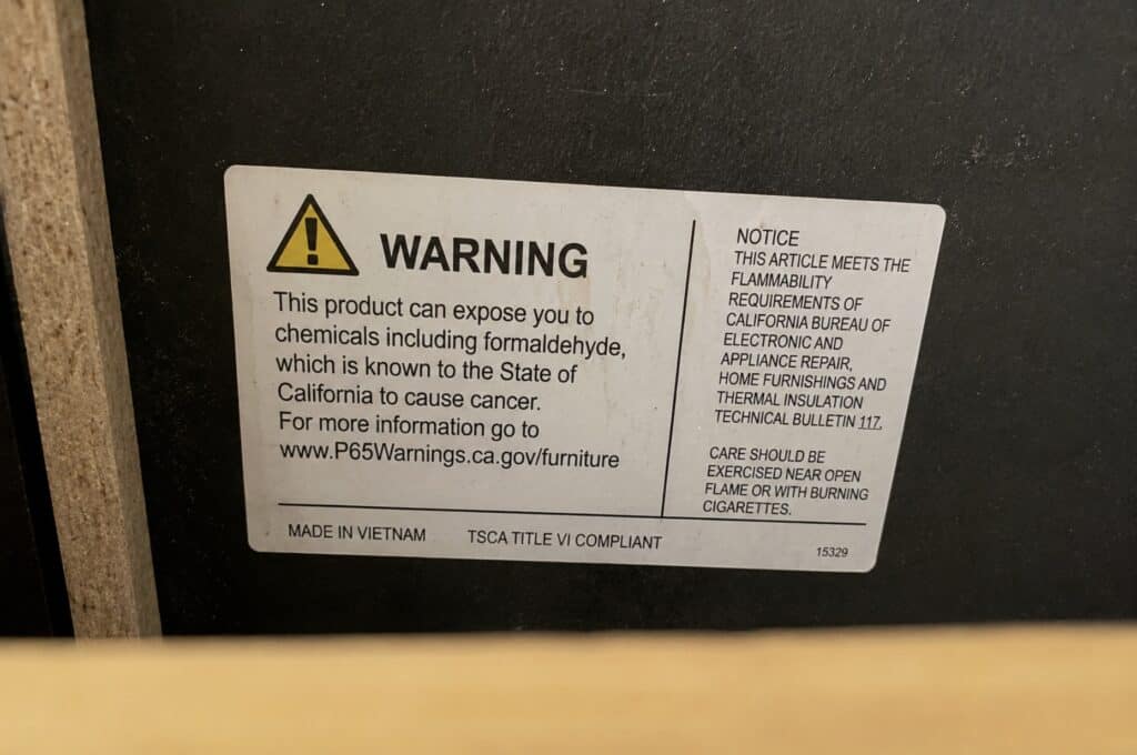 Close-up of a furniture label showing a Prop 65 warning and TSCA Title VI compliance information inside a wood furniture panel.