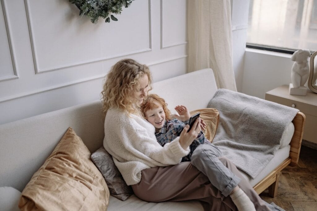 Mother and young child relaxing together on a light-colored upholstered sofa in a bright living room.