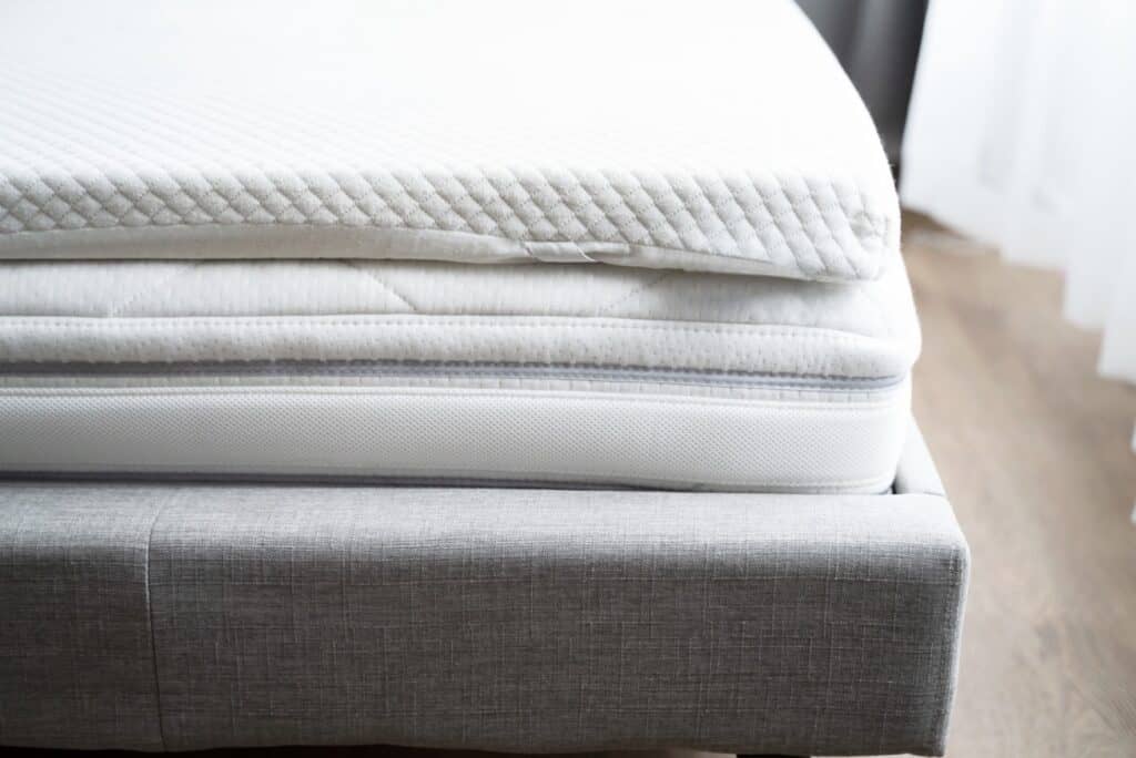 Mattress on a bed with the outer cover slightly lifted to reveal the foam layer inside.