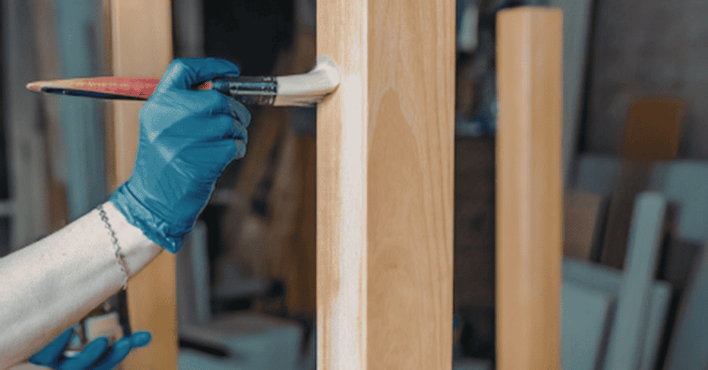 Person applying a protective finish to a natural wood furniture surface with a brush.