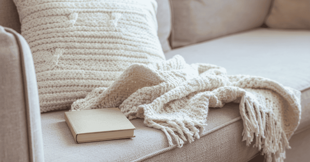 Close-up of soft sofa cushions with a knit blanket and pillow.