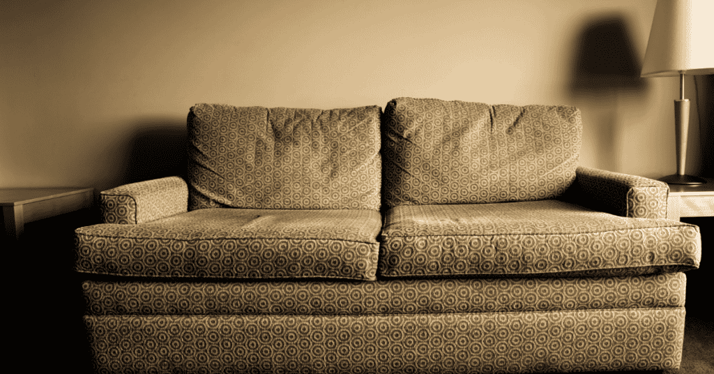 Old patterned sofa showing visible wear in a dimly lit room.