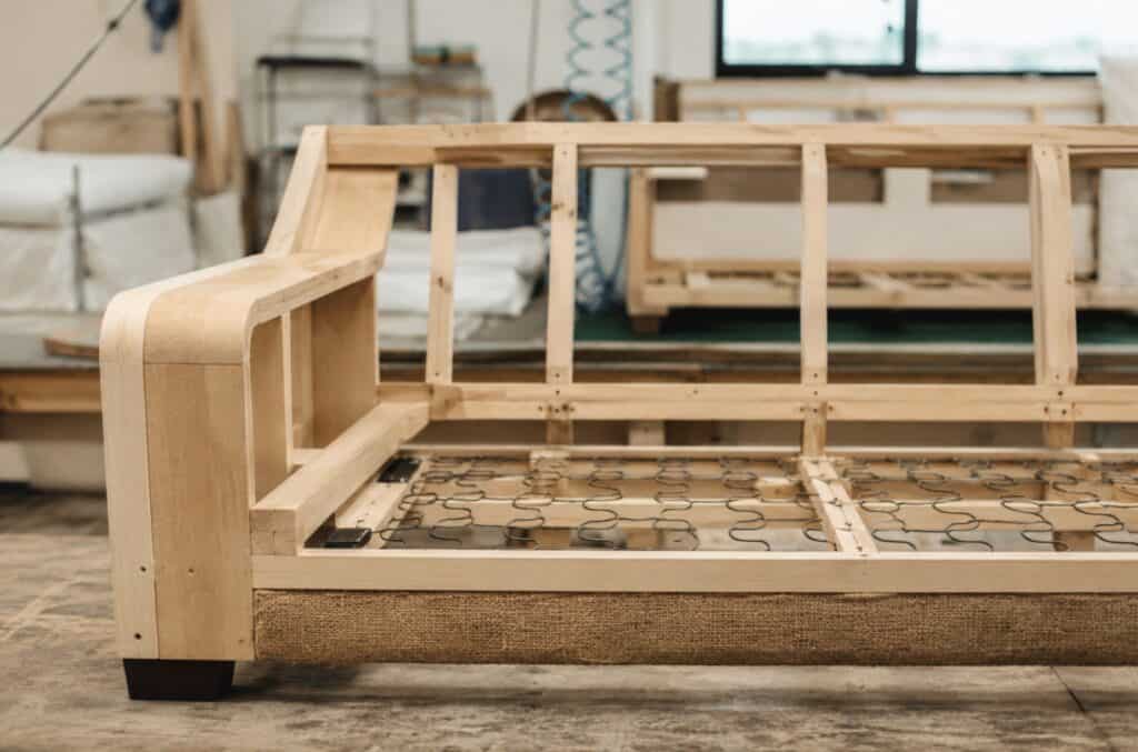 Exposed wooden couch frame in a furniture workshop showing the internal wood structure and support system before upholstery is added.