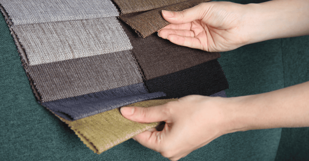 Hands compare neutral upholstery fabric swatches on a green sofa while choosing couch materials.