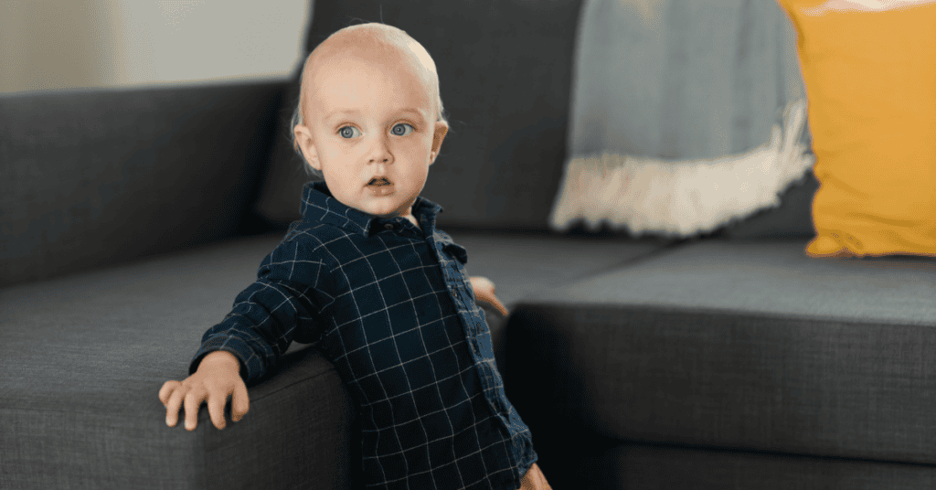 Toddler standing beside a gray fabric couch in a living room