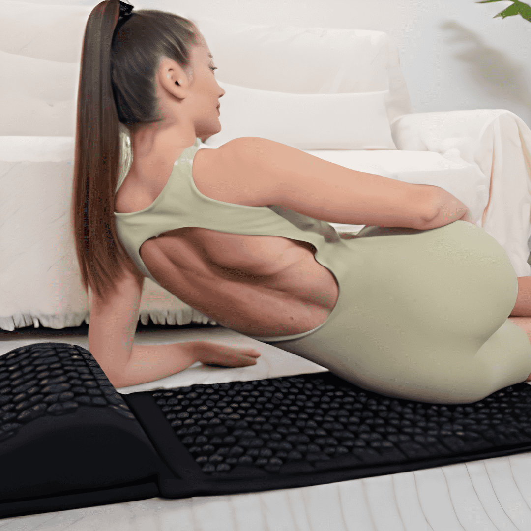 Woman in green activewear reclining on a black acupressure mat with a matching support pillow beside her.