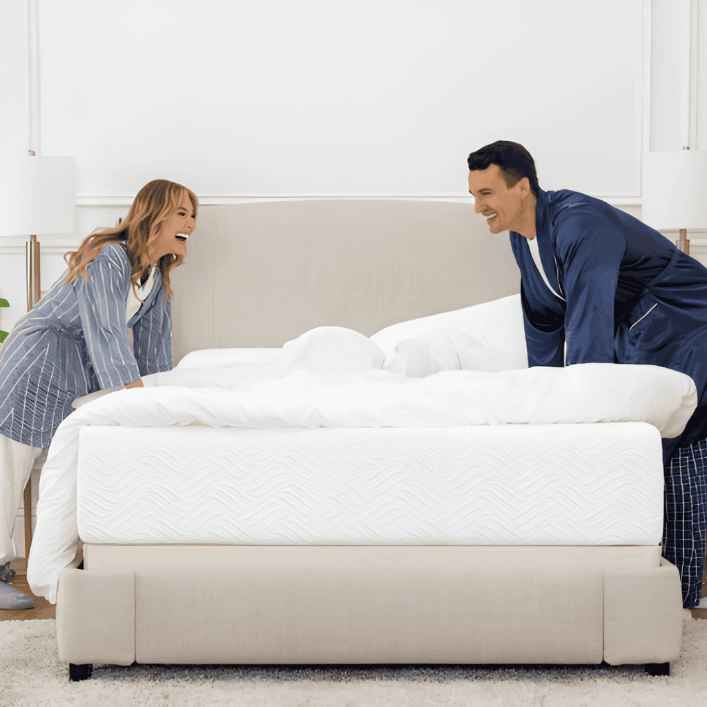 Couple lifting bedding over a white hybrid mattress in a bedroom.