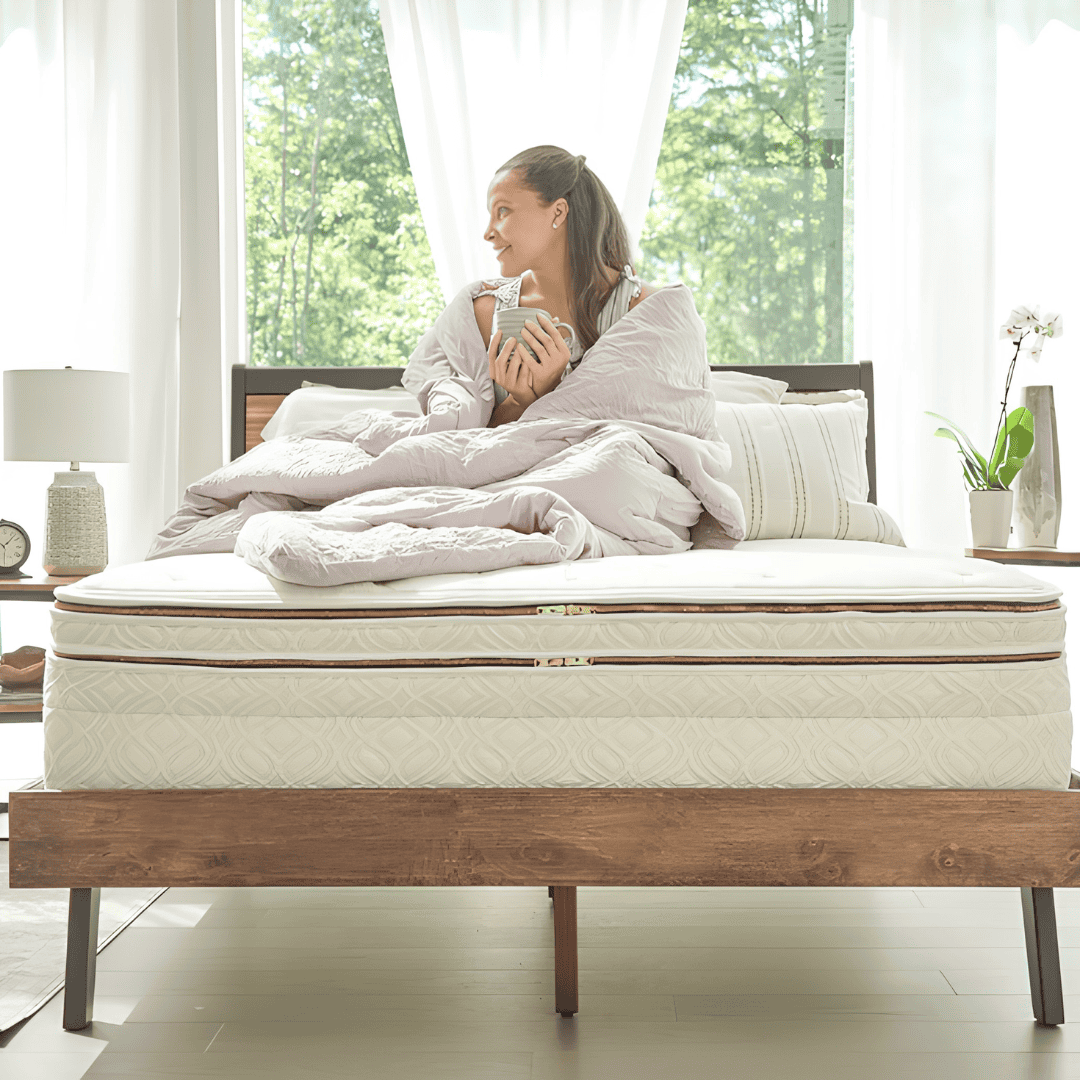 Woman relaxing with a mug on a layered organic mattress near a bright window.