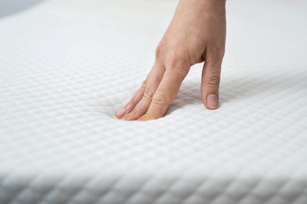 Hand pressing into a white quilted mattress.