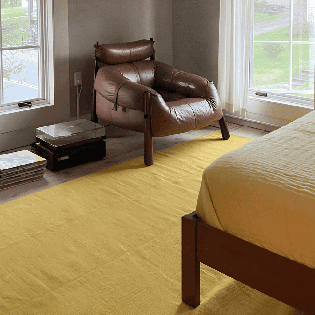 Mustard-yellow area rug beside a brown leather chair in a sunlit bedroom.