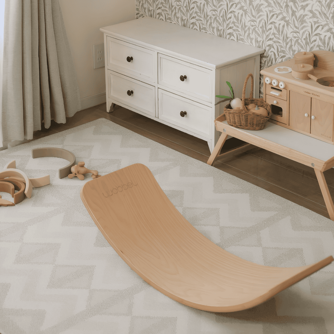 Neutral children’s playroom with a curved wooden balance board on a light geometric play mat.
