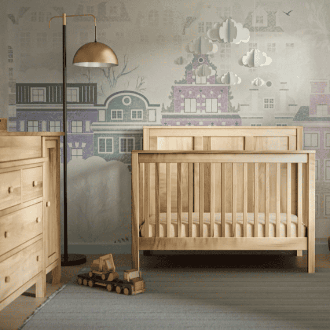 Natural wood crib and matching dresser arranged in a softly decorated nursery.