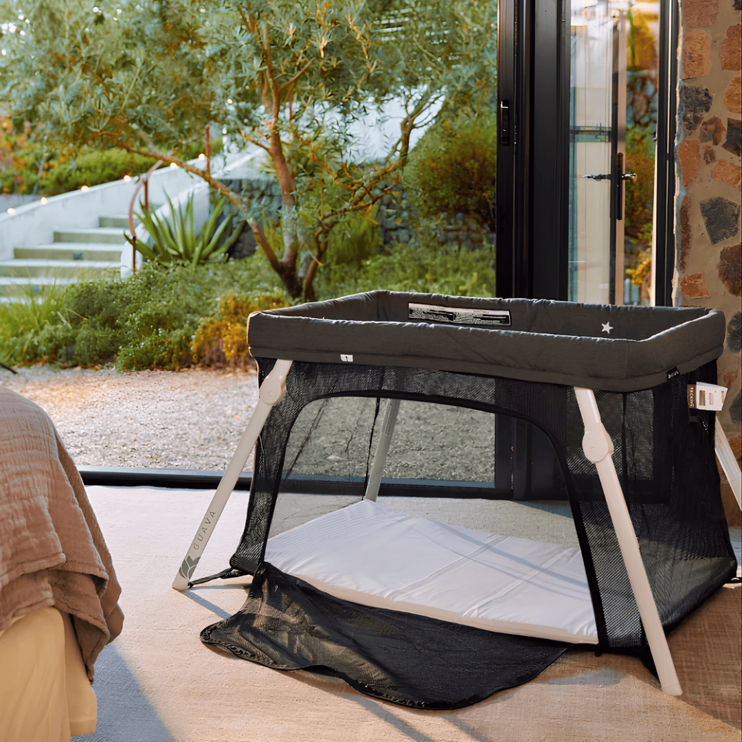 Guava Family Lotus travel crib with mesh sides and an open zippered door beside a garden patio.