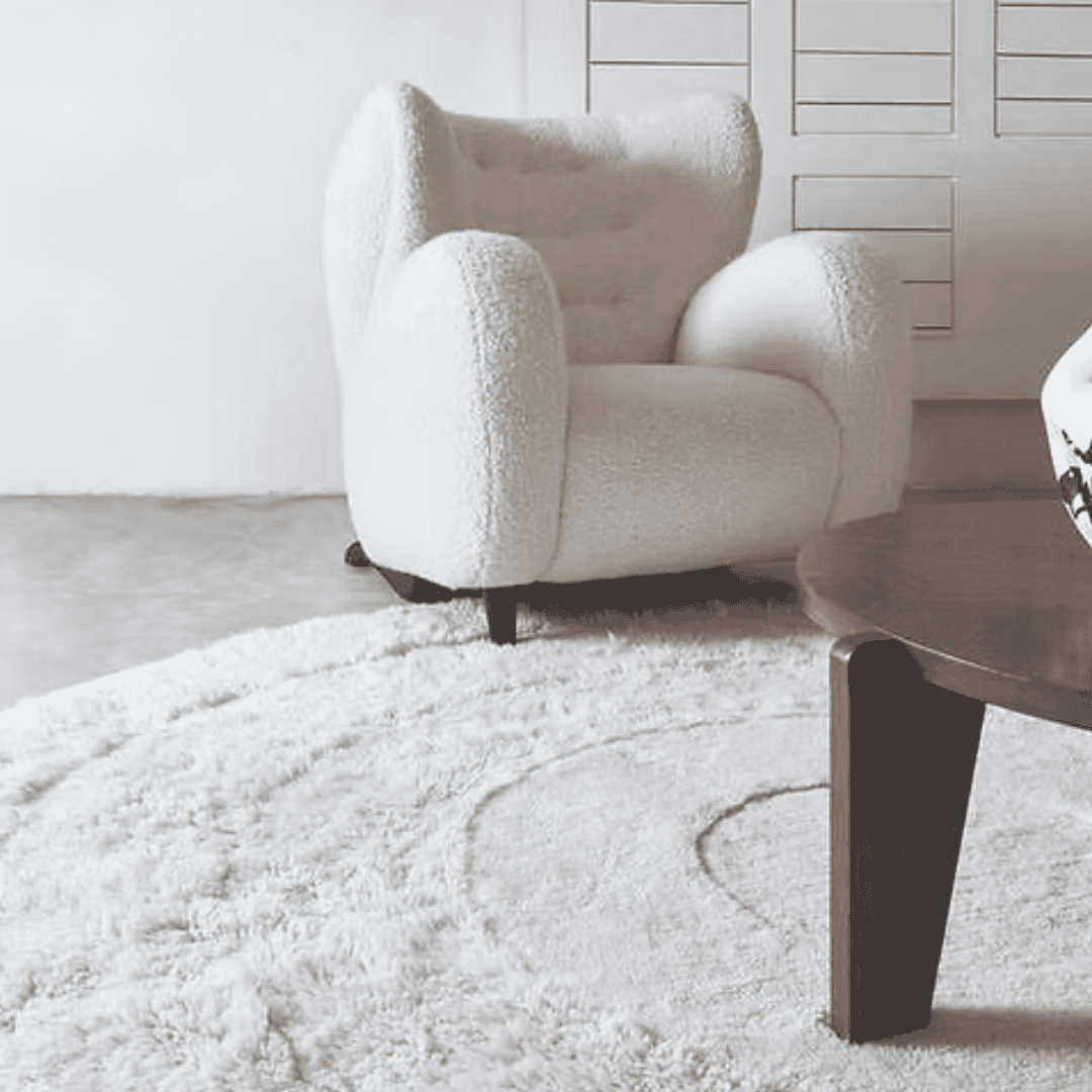 Soft white patterned rug beneath a cream armchair and wooden coffee table.