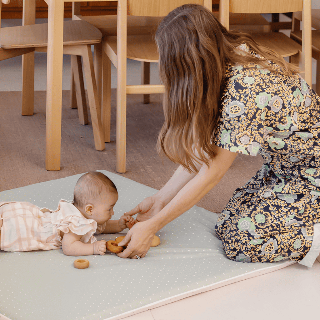 Parent playing with a baby during tummy time on a soft green Piccalio play mat.