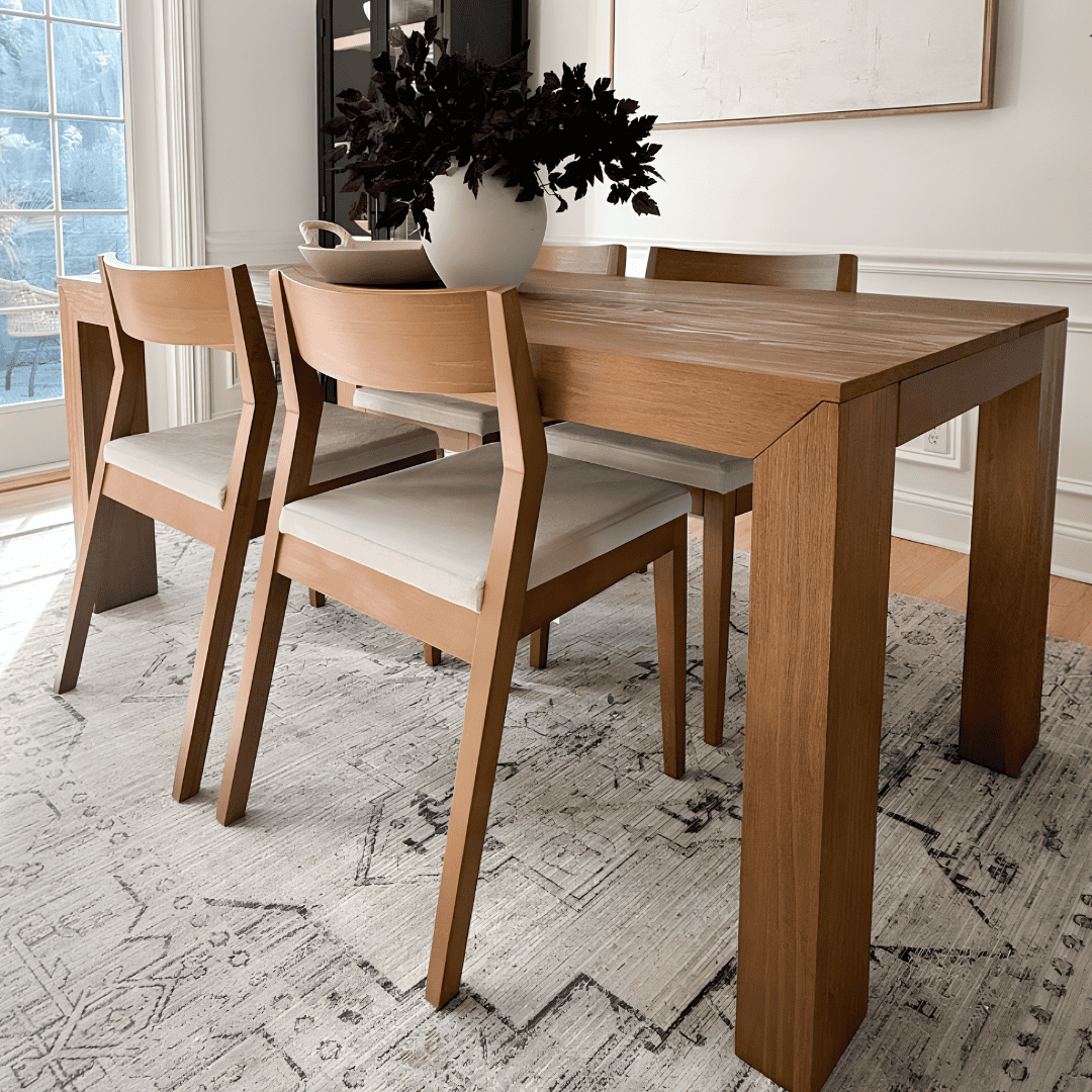 Wooden dining table with cushioned chairs in a naturally lit room.