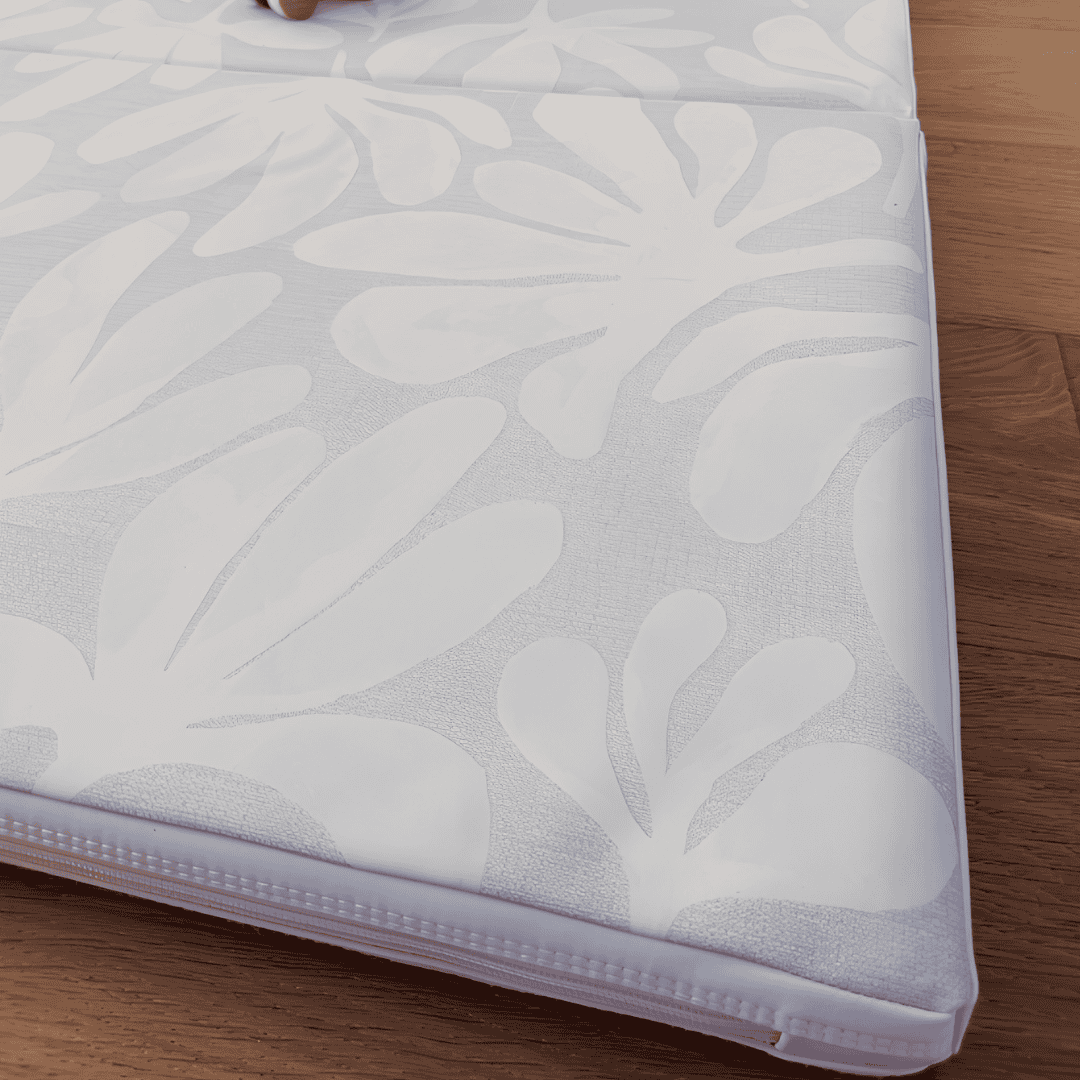 Close-up of a light gray Toddlekind play mat with a white botanical leaf pattern on hardwood flooring.