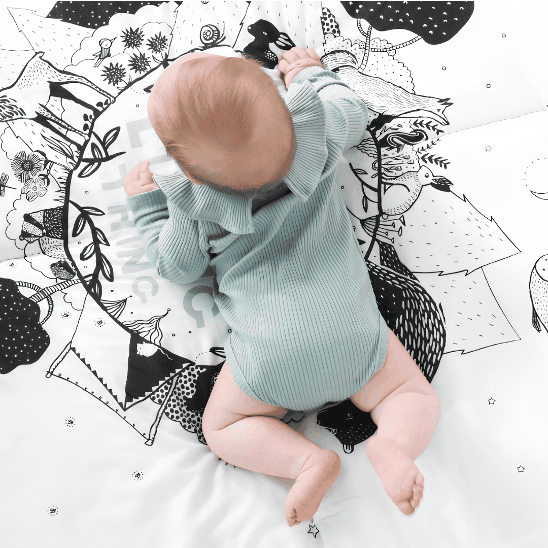 Baby lying on a black-and-white illustrated Wee Gallery play mat viewed from above.