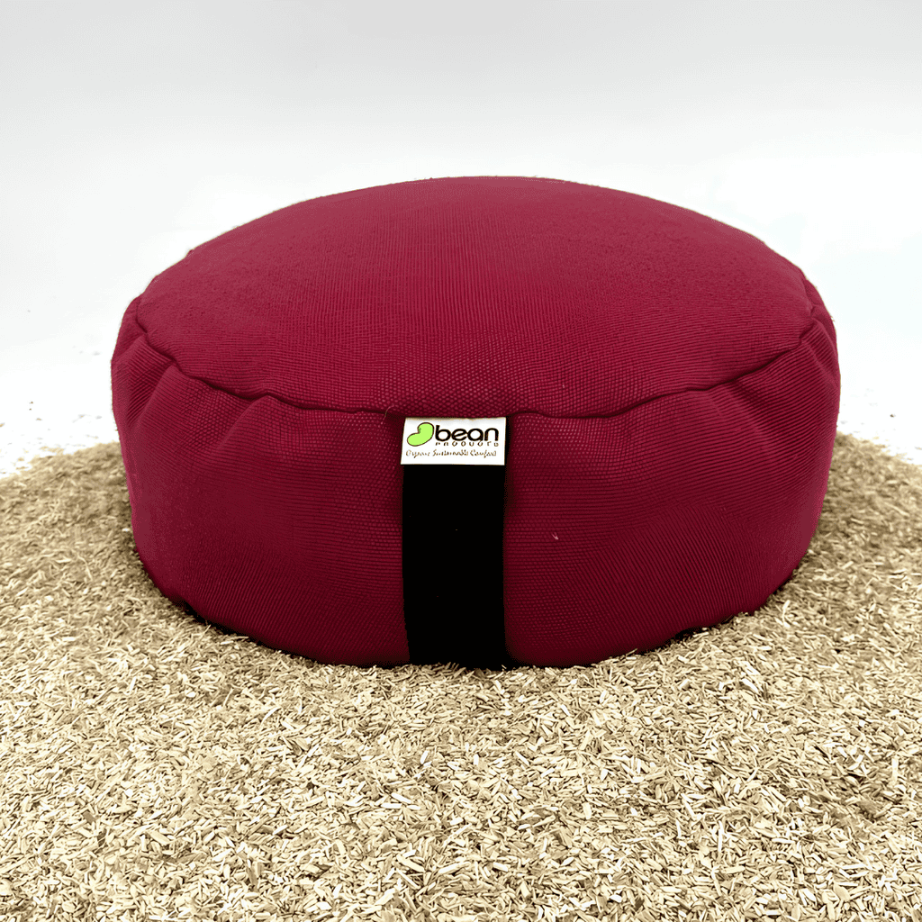 Burgundy round Bean Products meditation cushion displayed on loose buckwheat hulls.