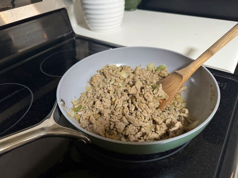Ground meat and vegetables cooking in a sage Caraway frying pan with a wooden spatula on a glass stovetop