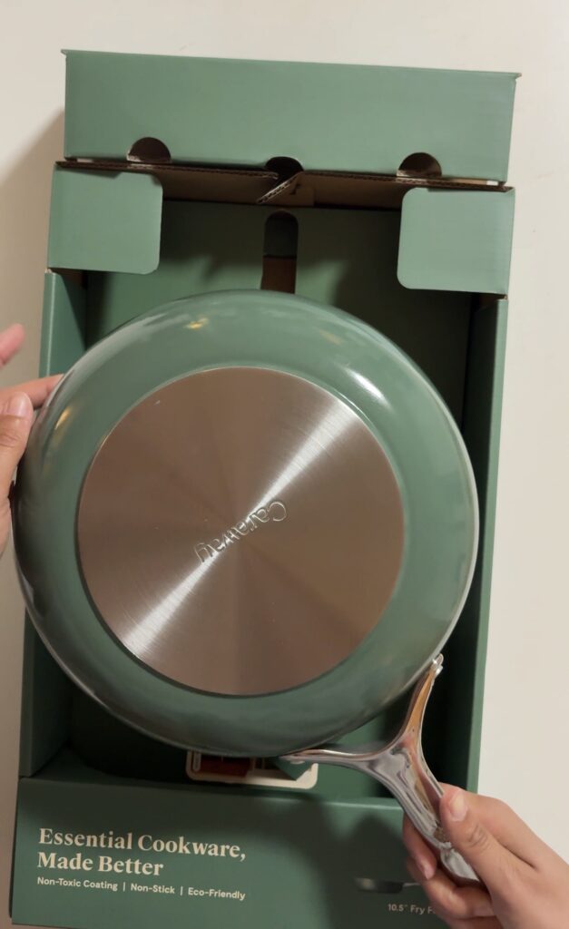 New sage Caraway frying pan held upside down over its open box, showing a clean, shiny metal base.