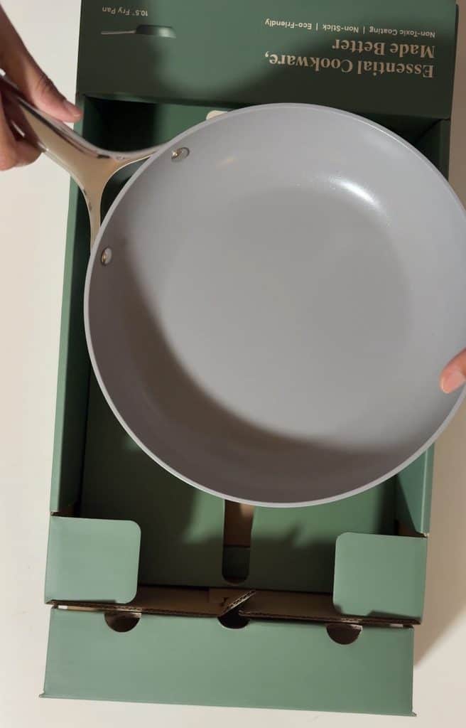 New Caraway frying pan held above its open box, showing the smooth gray ceramic-coated interior