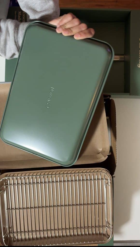 Hand holding a new Caraway baking sheet with its green underside facing the camera